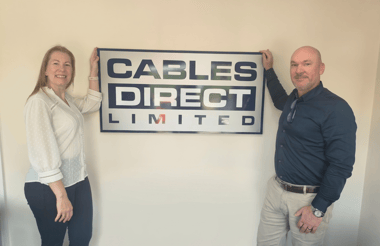Kelly Walker (left) and Jonpaul Warren (right) stand on either side of a “Cables Direct Limited” sign